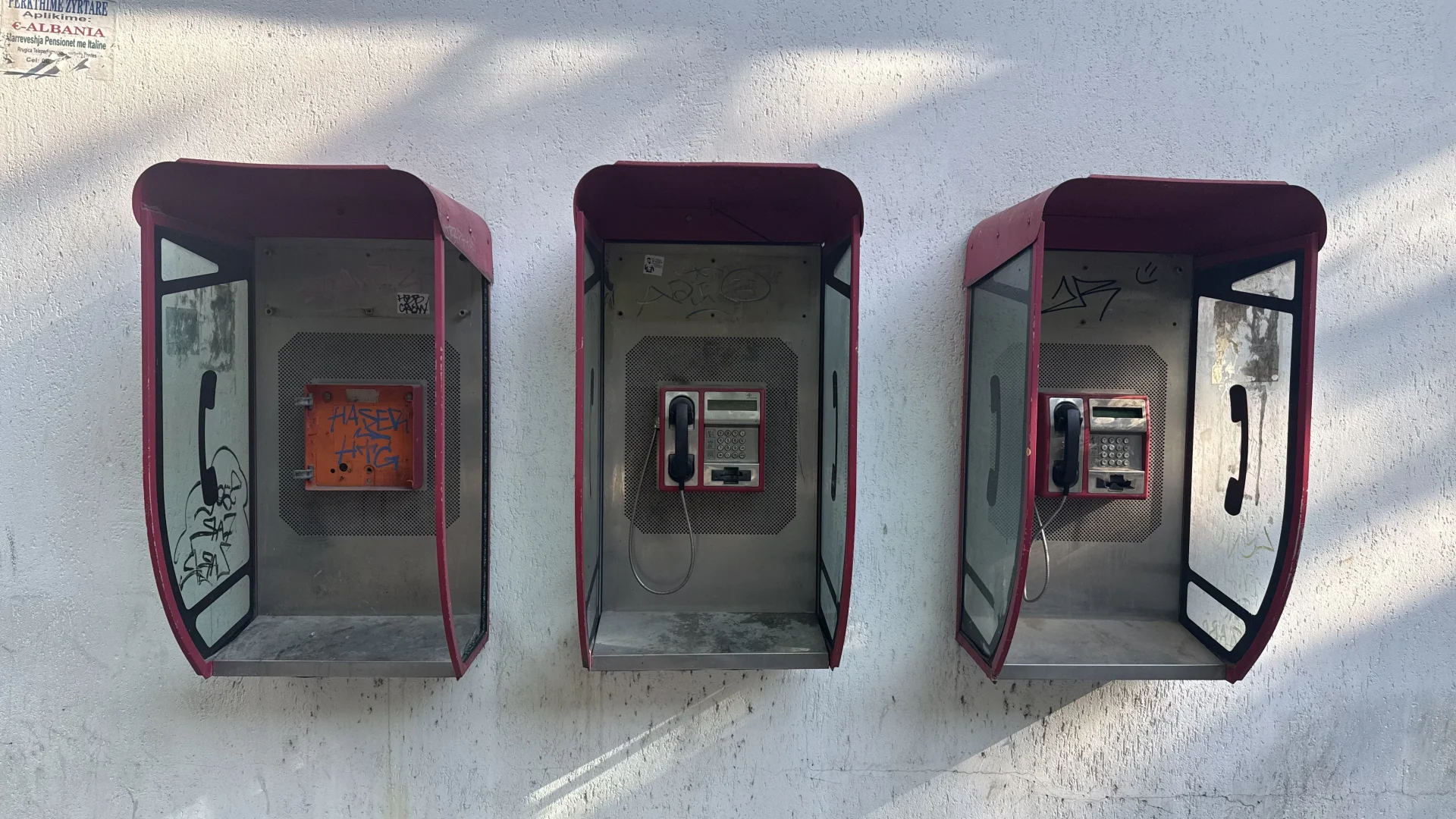 A row of colorful, weathered old phone booths along a street in Tirana, Albania, with buildings and passersby behind them. A nod to the jump from old-fashioned phone lines to the eSIM.