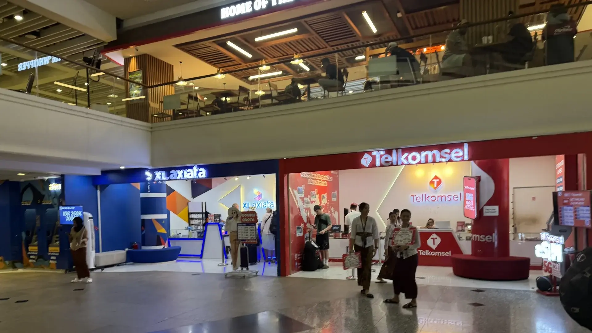The Telkomsel and XL Axiata mobile provider shops side-by-side in the arrivals hall of Bali's Ngurah Rai International Airport.