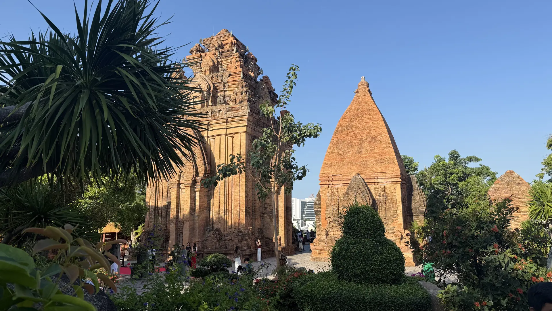 The brick towers of the Po Nagar Cham complex in Nha Trang, Vietnam, lit orange by the late afternoon sun above the tropical gardens below