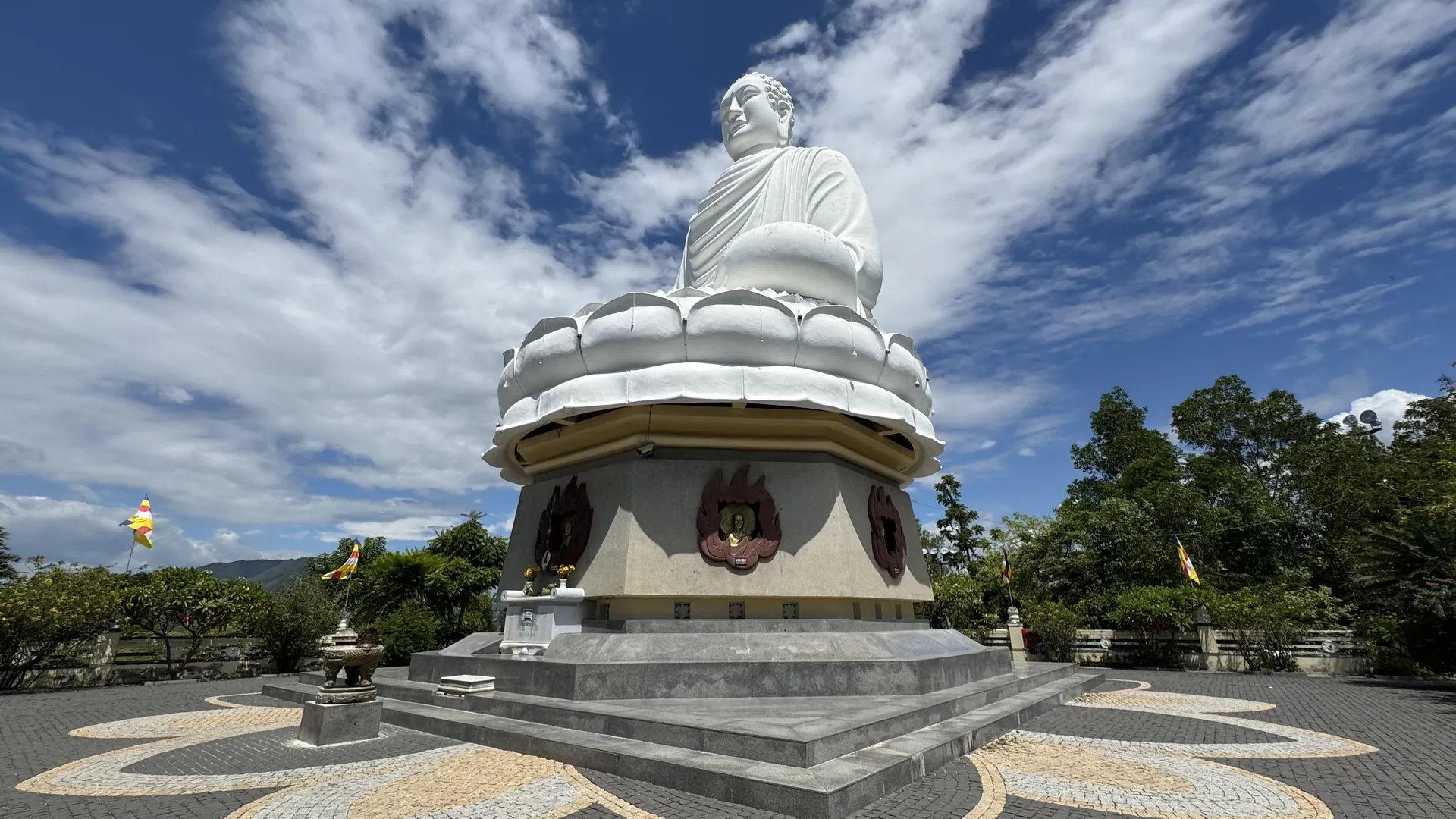 The white Kim Than Phat To Buddha seated on a lotus pedestal at Long Son Pagoda in Nha Trang, seen from the mosaic courtyard below against a blue sky