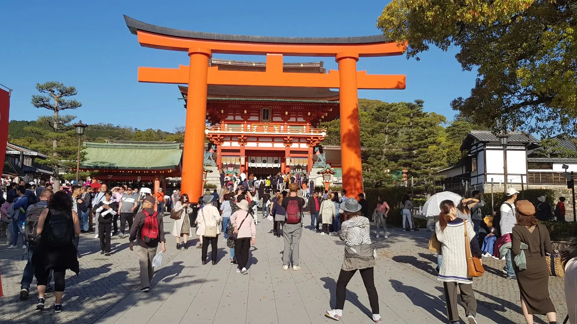 Crowds of tourists walking towards the famous orange torii gates at the entrance of Fushimi Inari Taisha shrine in Kyoto, Japan