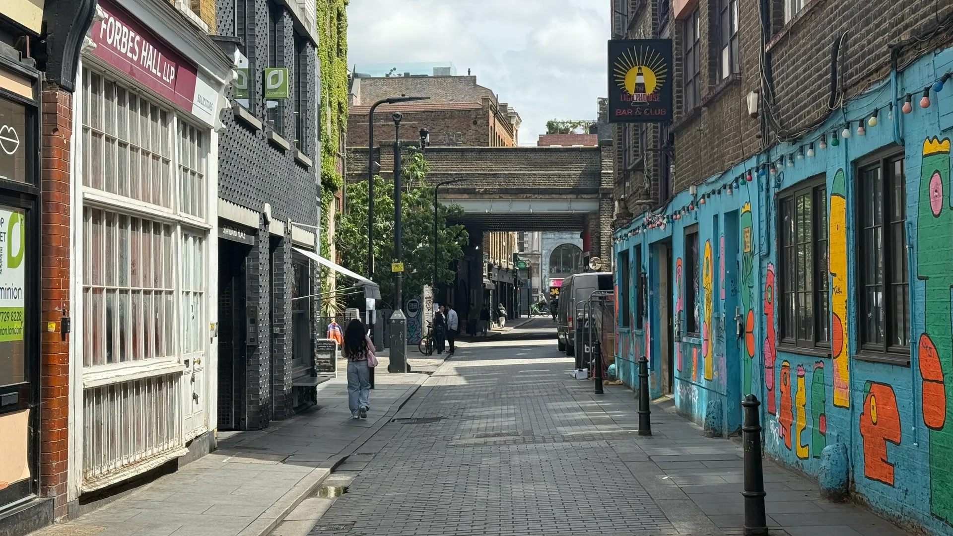 Side street in Shoreditch, London, with street art on a blue building, a brick railway bridge and the sign of the Lighthouse Bar & Club
