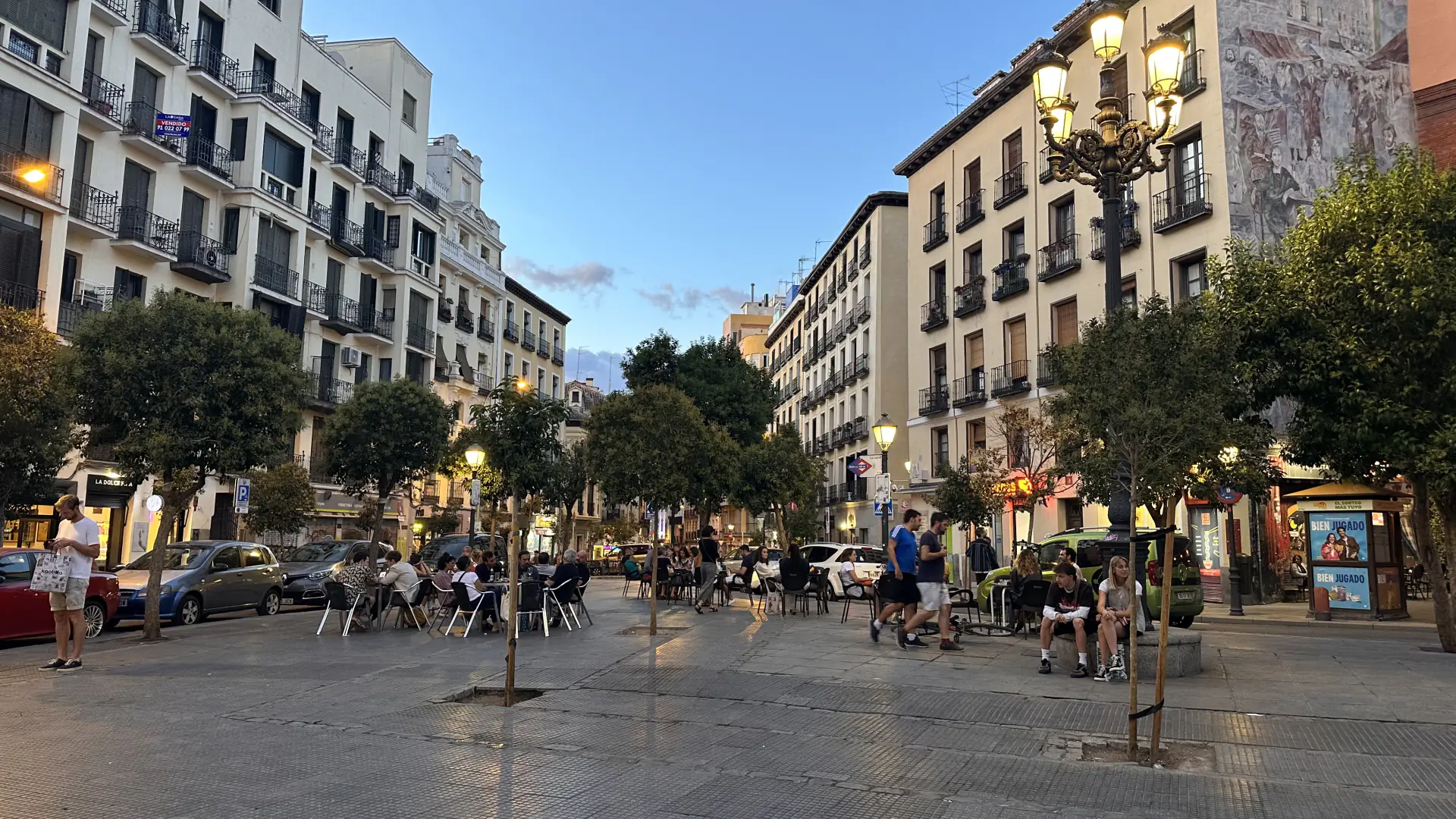 Evening on a tree-lined square in the La Latina district of Madrid, with busy outdoor terraces and lit street lamps