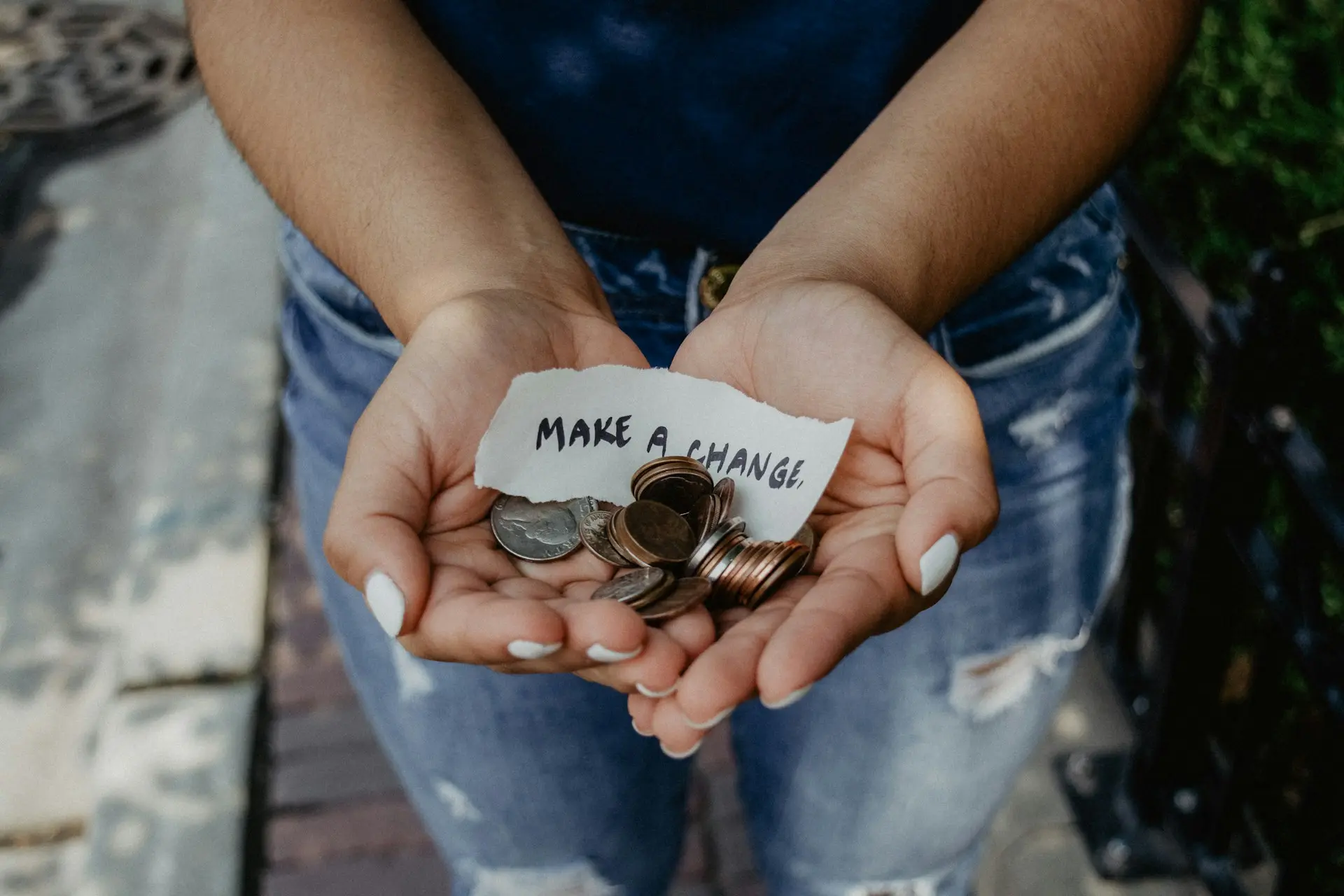 Illustration of making a positive impact: a person's hands holding a handful of coins and a small note that says 'Make a Change'.